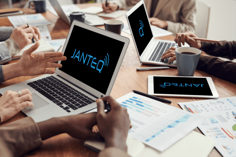 cluttered table with laptops displaying "Janteq"